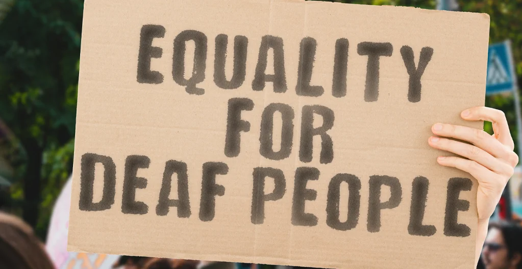 A Caucasian man’s hand holding a banner with the text ‘Equality for deaf people.’ 