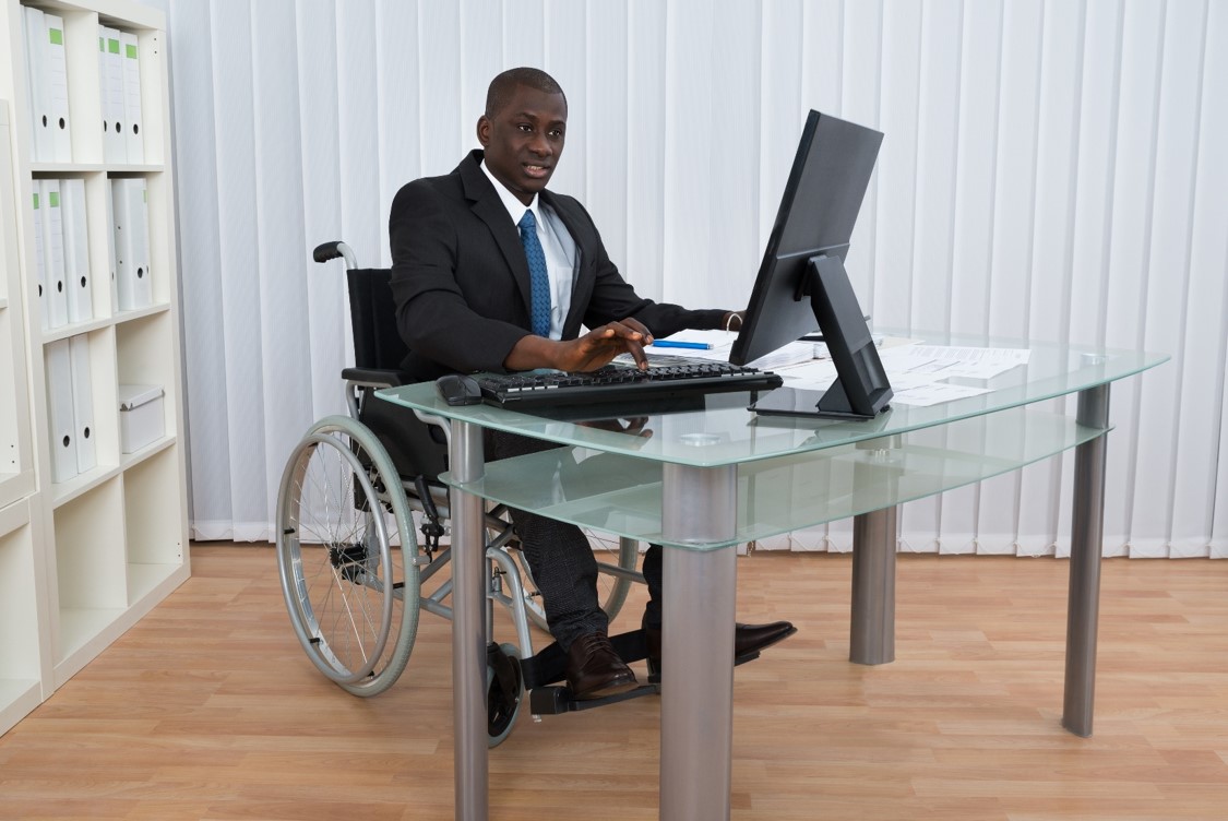 Blind man in a wheelchair works at an office computer.