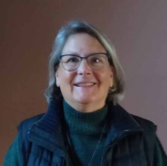 Photo of Susan, a woman with light silver hair almost to the top of her shoulders, glasses, and smiling at the camera. 