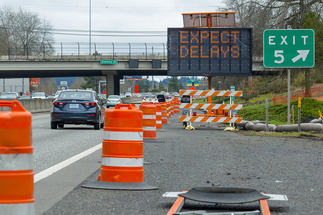 Highway with construction barrels and illuminated expect delays board.