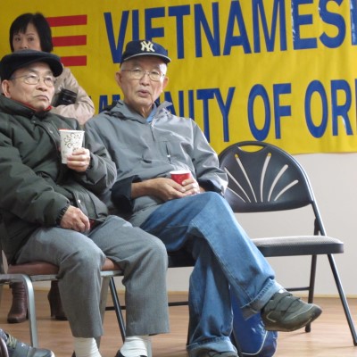 Two community members sit in folding chairs at an indoor event.