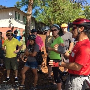 Community members wearing bike helmets gather on a sidewalk and listen to an odot worker.