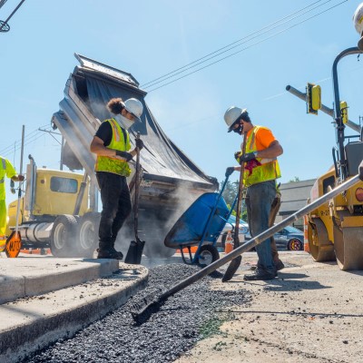 A dumptruck emptying gravel while two ODOT workers use shovels to spread the gravel.