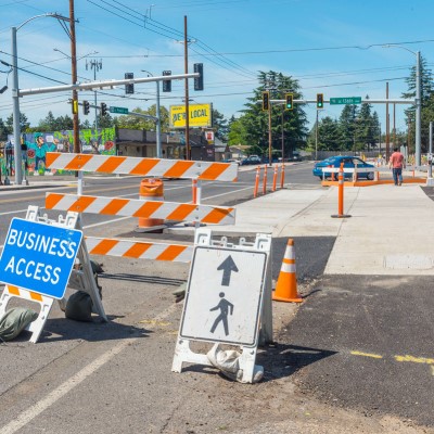 A sidewalk that is blocked off due to construction with a sign directing pedestrians down a temporary pedestrian pathway.