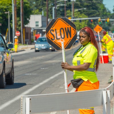 A female ODOT worker stands on a street holding a 