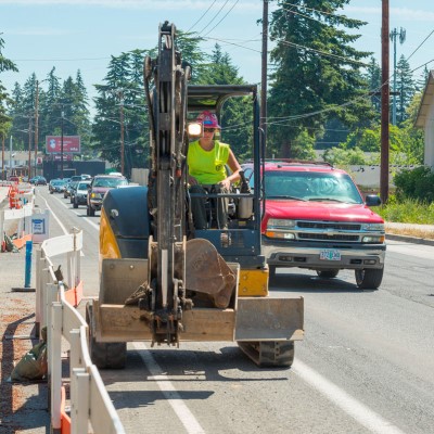 An ODOT worker is driving a backhoe along a local road.