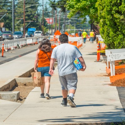 Two pedestrians walk down a temporary pedestrian walkway in a construction zone.