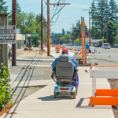 A pedestrian with a motorized wheelchair on a temporary pedestrian walkway in a construction zone.