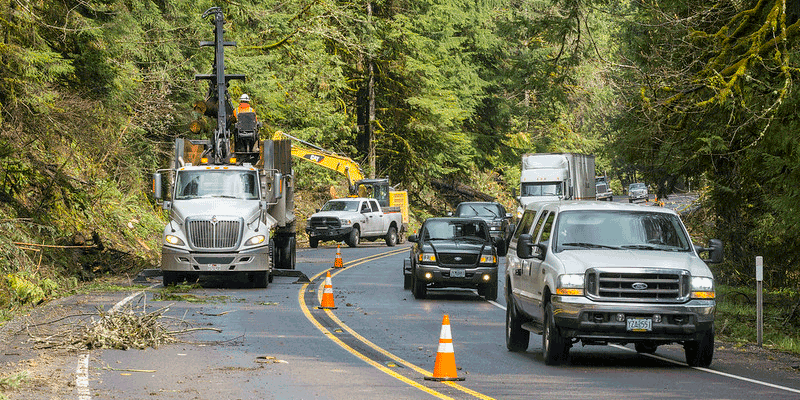 ODOT employess clearing debris off road after storm while traffice drives past.