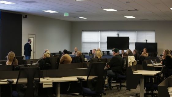 A crowd of people sitting at tables and looking at a TV screen near a window