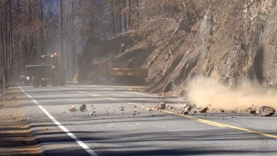 Rocks from a mountain falling on a road with smoke in the air