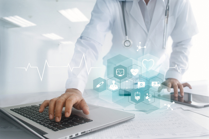 Health care provider leaning over table and typing on laptop